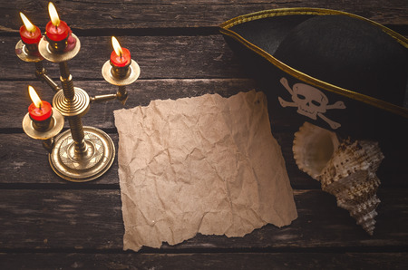 Blank crumpled paper page with copy space for pirate treasure map on captain table with pirate hat, seashell and candle.の写真素材
