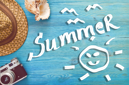Summer background with copy space. Retro photo camera, seashell and hat on blue wooden background.の写真素材