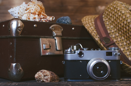 Retro summer sea vacation background. Vintage suitcase, film camera, hat and seashells on tourist table. Front view, close up photo.の写真素材