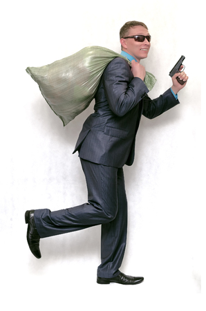 Robber man is running away from bank with money bag and pistol in hands isolated on white background. Financial fraud.の写真素材