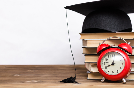 Stack of books, graduate cap and red alarm clock on the school desk isolated on white background.の写真素材