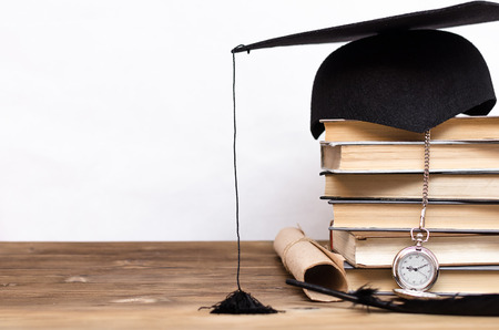 Stack of books, graduate cap, diploma and pocket watch on the school desk isolated on white background.の写真素材
