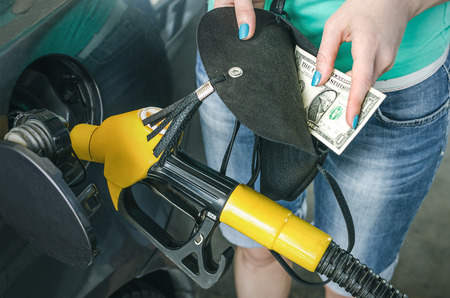 Expensive gasoline. Lack of money for gasoline and fuel. Driver holds one dollar end empty wallet on background of a fuel nozzle in the gas tank. Increase in gasoline prices concept.の写真素材