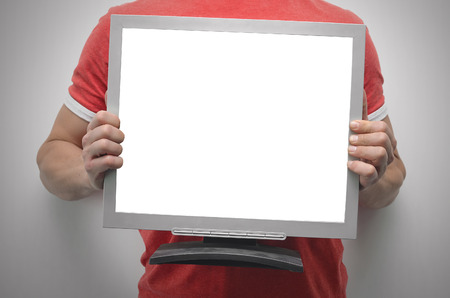 Man is holding a computer monitor with blank screen in front of him isolated on gray background.の写真素材