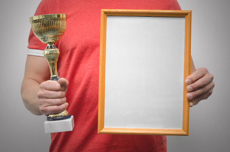 Man is holding a blank diploma or certificate frame with copy space and golden award trophy in the...