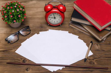 Blank exam tickets, books, school pointer, glasses and a red alarm clock on the school desk in the...