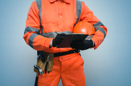 The measurer worker writes dimensions to his notebook. Building contract signing. Builder with construction project plans in the hands isolated on blue background.の写真素材