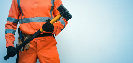 Builder worker holding in hands a big sledgehammer isolated on blue background with copy space....