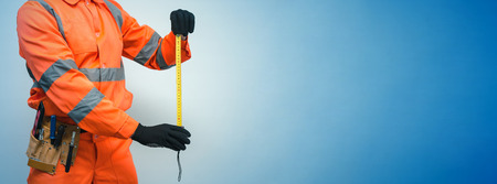 Builder worker makes a measurement by building tape isolated on blue background with copy space. Under construction concept background.の写真素材