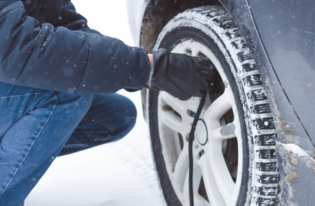 Driver is inflating a tire by car air compressor on the winter road.の写真素材