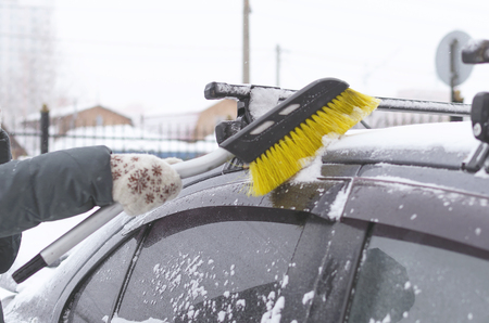 The driver cleans the car from the snow with a brush on the winter street.の写真素材