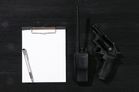 Blank paper page, pen, portable radio station and handgun on a black background. Top secret document mockup. Detective agent dossier. Interrogation report.の写真素材
