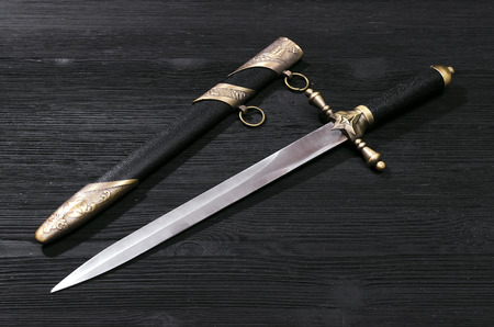 Dagger knife isolated on the black wooden background.