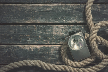 Rope and retro flashlight on the wooden table surface background with copy space. Adventurer or treasure hunter desk.の写真素材