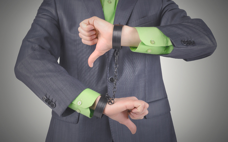 Handcuffs on a businessman hands isolated on a gray background.の写真素材