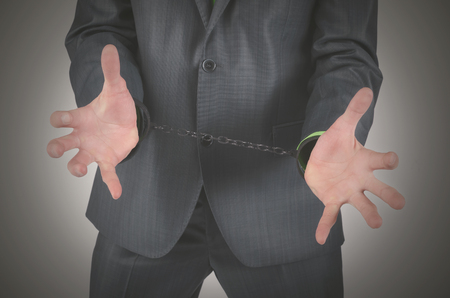 Handcuffs on a businessman hands isolated on a gray background.の写真素材