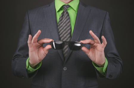 Black sunglasses in a businessman hands on a black background. Conspiracy concept.の写真素材