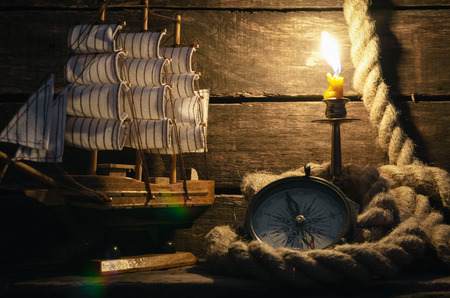 Marine ship, mooring rope, compass and burning candle on a captain table background. Sea travel or...