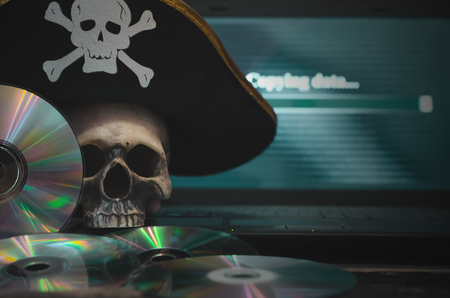 Illegal data copying concept. Cybercrime. Computer piracy background. Pirate hat, human skull, laptop and compact disc on a table.の写真素材