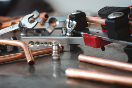 Pipes, pipe bender and other pipework tools on a fitter workbench background.