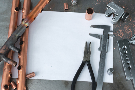 Brass pipes, pipe cutter, calipers, pliers and a blank layout drafts of pipeline system on a fitter workbench.の写真素材