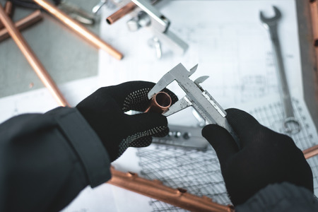 Engineer is holding in hands a brass pipe and is measuring a diameter by a calipers. Pipework.の写真素材