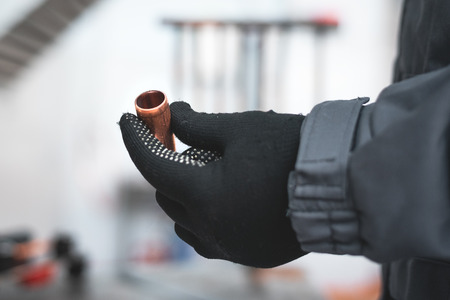 Worker is holding in hands a brass pipe trimming on a fitter workbench background. Pipework.の写真素材