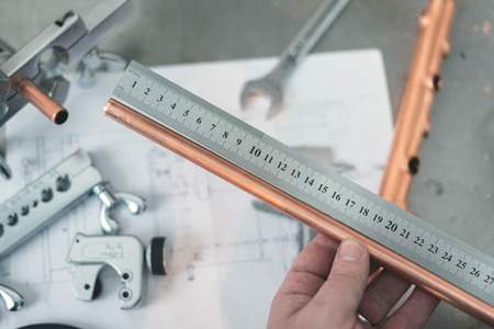 Worker is measuring a pipe by a straightedge on a fitter workbench background. Pipework.