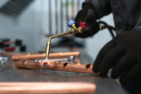 Worker is soldering a pipe by a blow lamp on a factory workbench background. Pipework.の写真素材