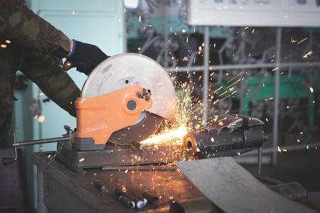 Worker cuts a pipe on circular saw on the workbench in the workshop. Metalworking.