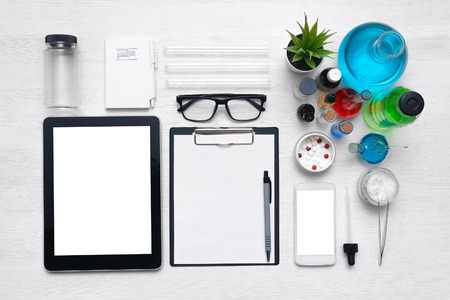 Tablet computer and mobile phone with blank screen, blank paper sheet with copy space, various drugs on a laboratory table background. Medicine, pharmacology or pharmacy background.の写真素材