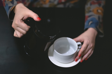 Woman is pouring a hot tea from teapot to a cup.の写真素材