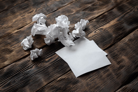 Blank paper sheet and crumpled pages around on a wooden board background.