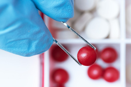 A red medical tablet in a forceps in a hand of doctor. Medicine, pharmacology, pharmacy background.の写真素材
