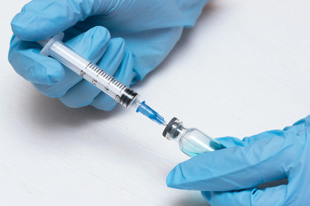 Syringe and a bottle with a blue liquid in a doctor hands in a medical gloves. Medicine background.の写真素材