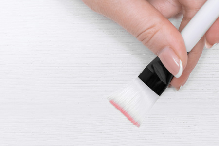Make up brash in a female hand on a white wooden table background.の写真素材