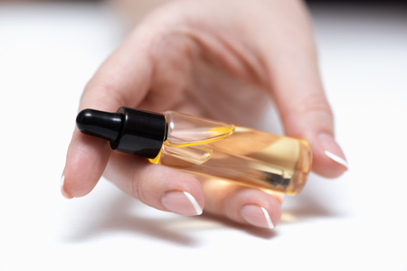 Yellow cuticle oil bottle and a female hands on a white wooden table background. Fingernail care concept.の写真素材