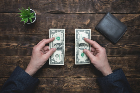 Business man is holding in hands a empty wallet with few dollars. Tight of money. Lack of money. Financial problems. Bankrupt. Pay the bill concept.の写真素材