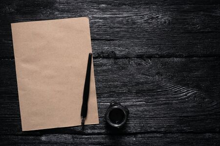 Brown blank paper page with a copy space, quill pen and a inkwell on a black wooden table flat lay background.の写真素材