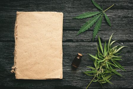 Cannabis cbd oil recipe blank book with a copy space, cbd oil in a bottle and green leaves on a black wooden table background.の写真素材
