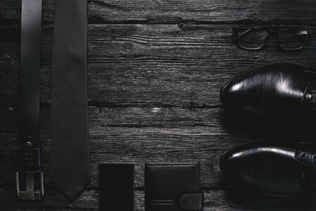 Business flat lay background with a copy space. Male shoes, belt, mobile phone, wallet, glasses and a necktie on black wooden floor.の写真素材
