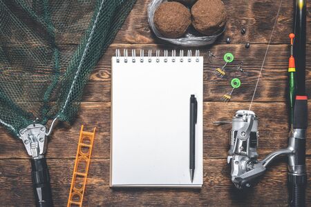 Fisher book template or fishing tips. Fishing gear and a blank page notepad with a copy space on wooden background.の写真素材
