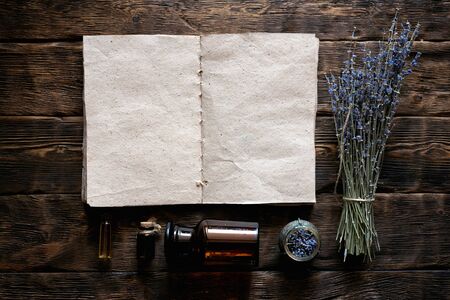Dried lavender flower branches, lavender essential oil bottles and a blank aromatherapy recipe book...