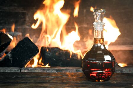 Strong alcohol in a transparent bottle on a wooden table on a burning fire background.の写真素材