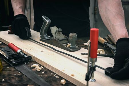 Worker is take a measurements with a construction meter of a wooden bar on his workbench.