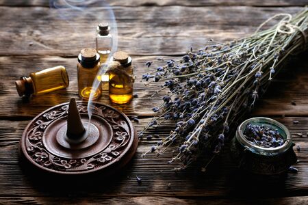 Dried lavender flower branches and lavender essential oil bottles on a wooden table background....