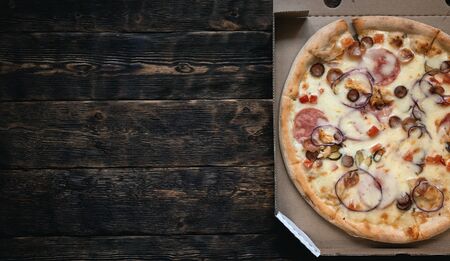 Fresh pizza with cheese and sausage in a cardboard box on a brown wooden table background with a copy space.の写真素材