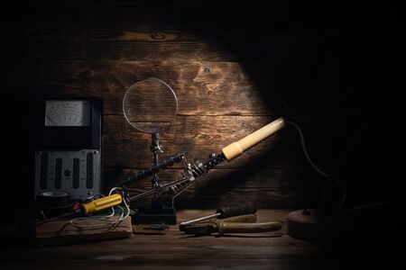 Retro analog voltmeter, soldering iron,handbook, microcircuit, pliers and screwdriver in the light...