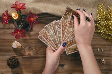 Tarot cards and hands of fortune teller on wooden table background.