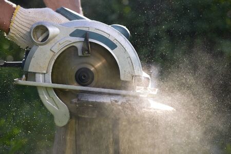 Man is cutting a timber by a circular saw in his hand.